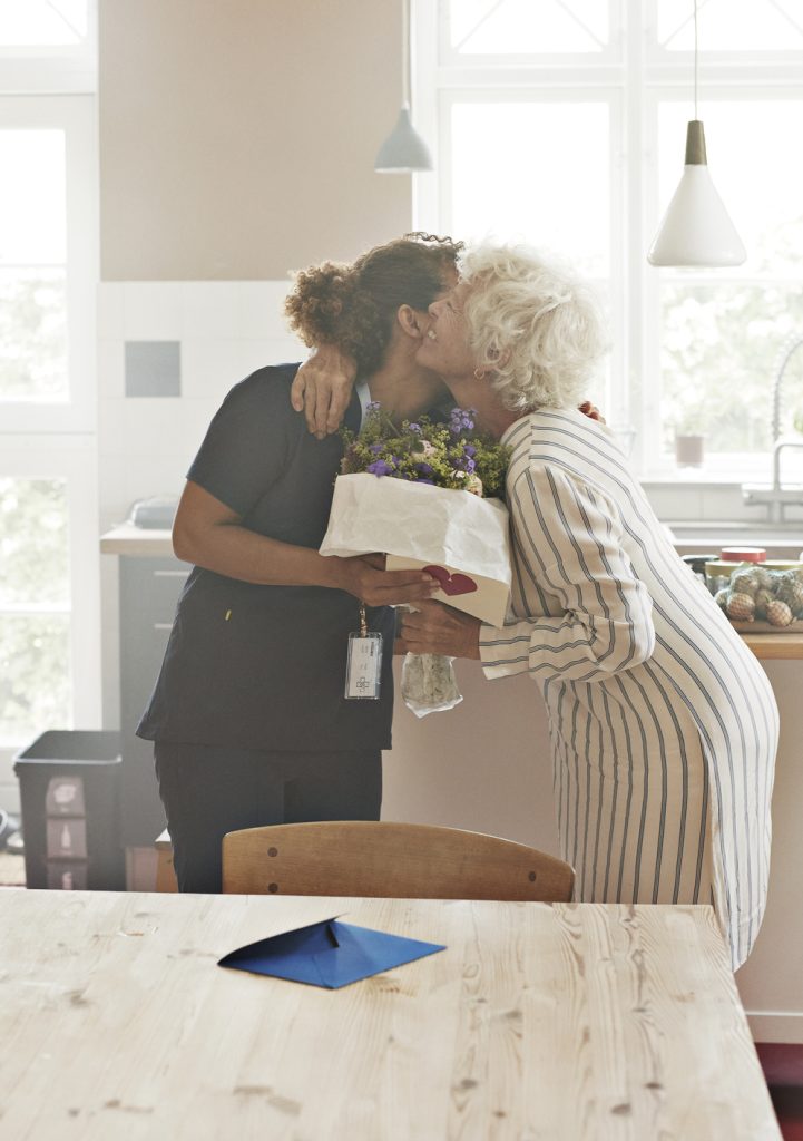 Senior woman greeting caregiver with bouquet